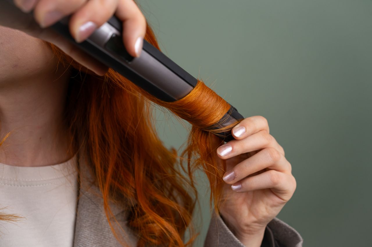 heros-img Close-up of a woman curling her vibrant red hair with a curling iron.
